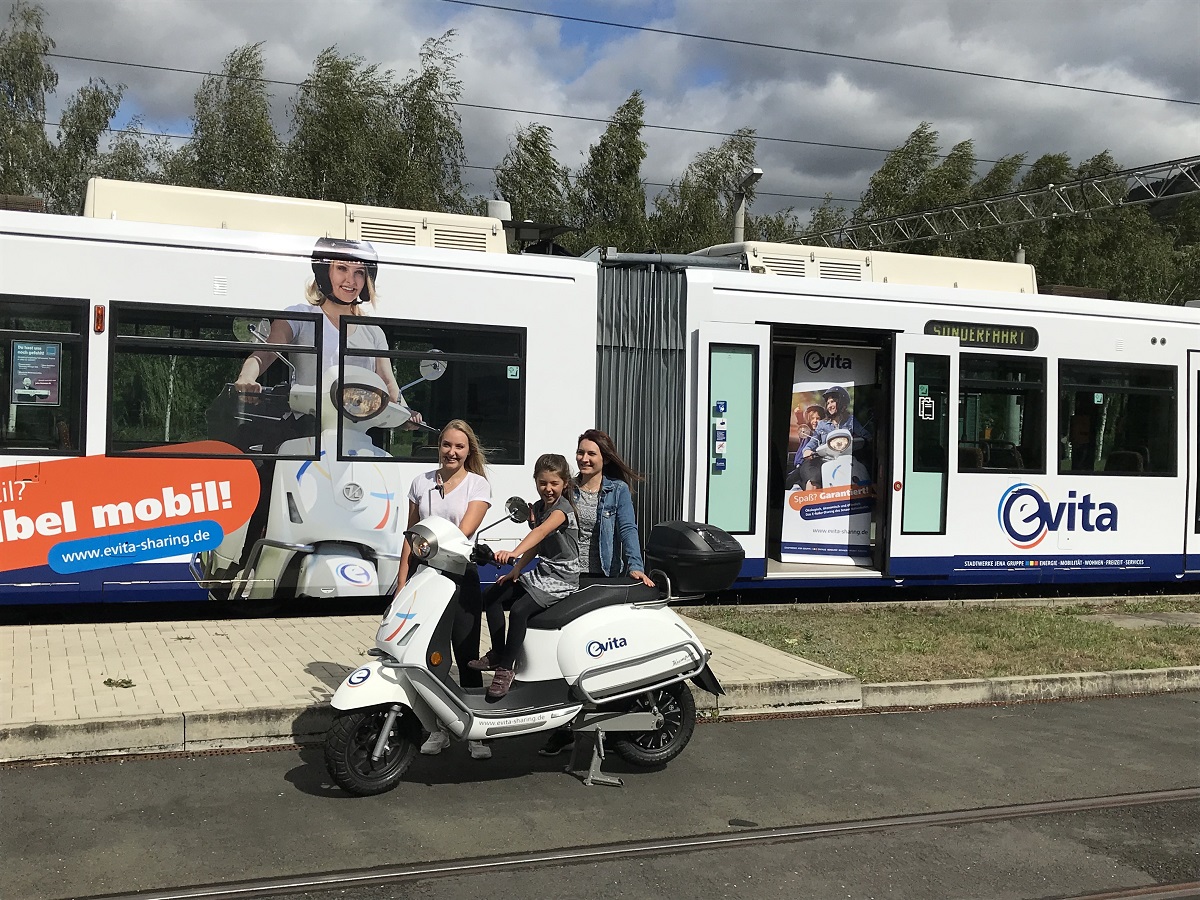Die Fotomodels der evita-Kampagne mit einem der E-Roller vor der zu präsentierenden evita-Straßenbahn