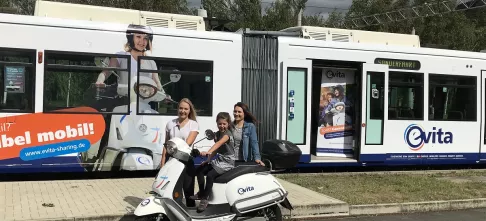 Die Fotomodels der evita-Kampagne mit einem der E-Roller vor der zu präsentierenden evita-Straßenbahn