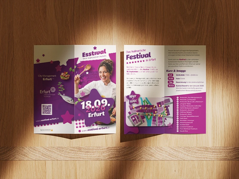 Drei gestaltete Esstival-Flyer mit Veranstaltungsinformationen und Programmübersicht vor einem warmen Holzhintergrund