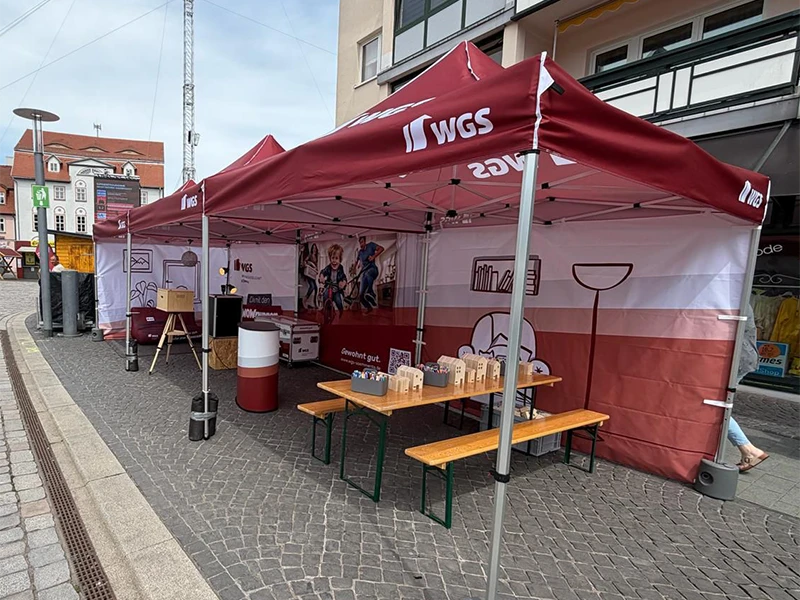Gesamtansicht des rot-weißen WGS-Pavillons auf dem Marktplatz in Sömmerda mit Infotheke, Sitzbänken und Werbemitteln.